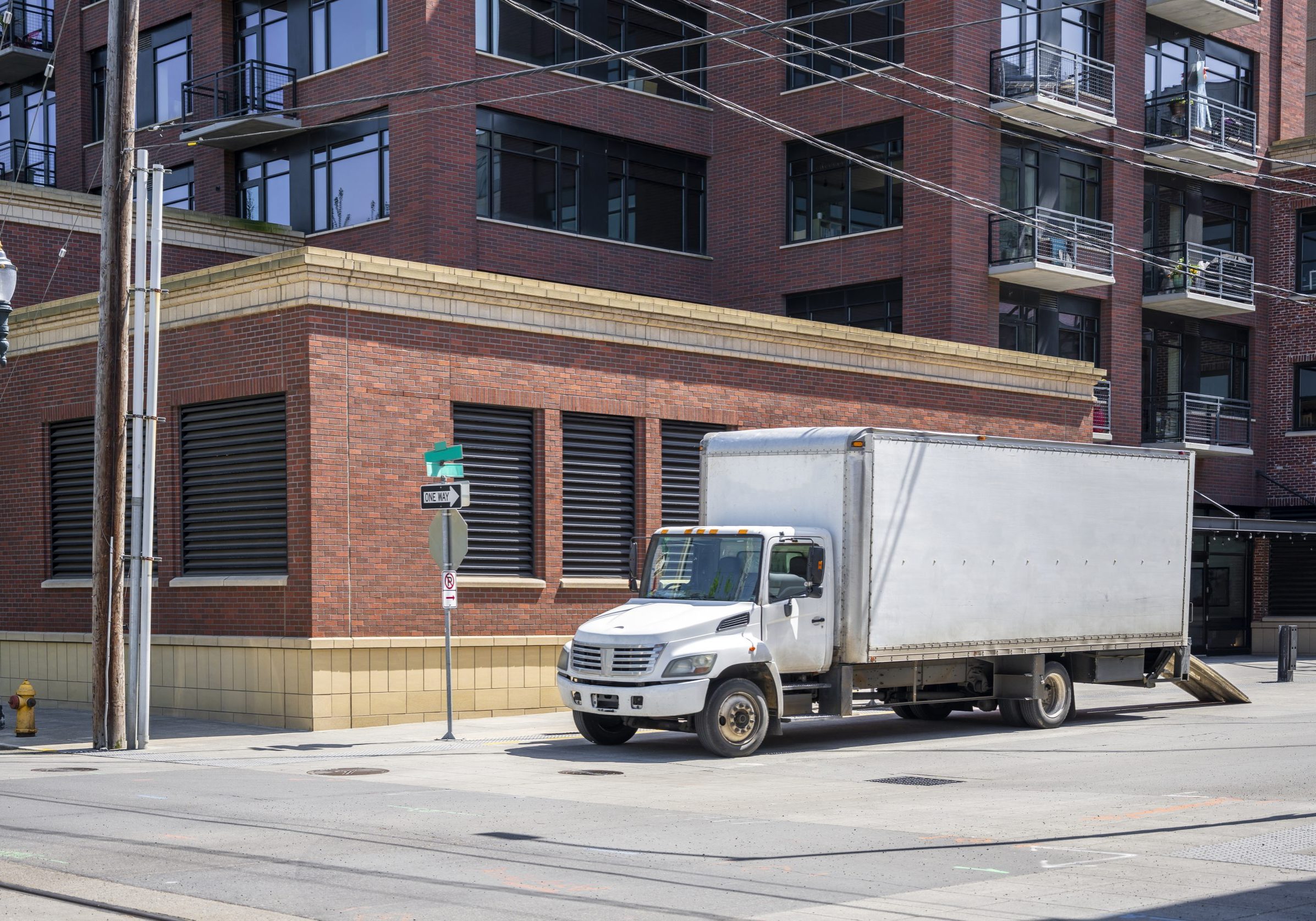 Compact rig semi truck with box trailer for moving to new apartments and local deliveries standing on the city street with multilevel apartment buildings for loading goods
